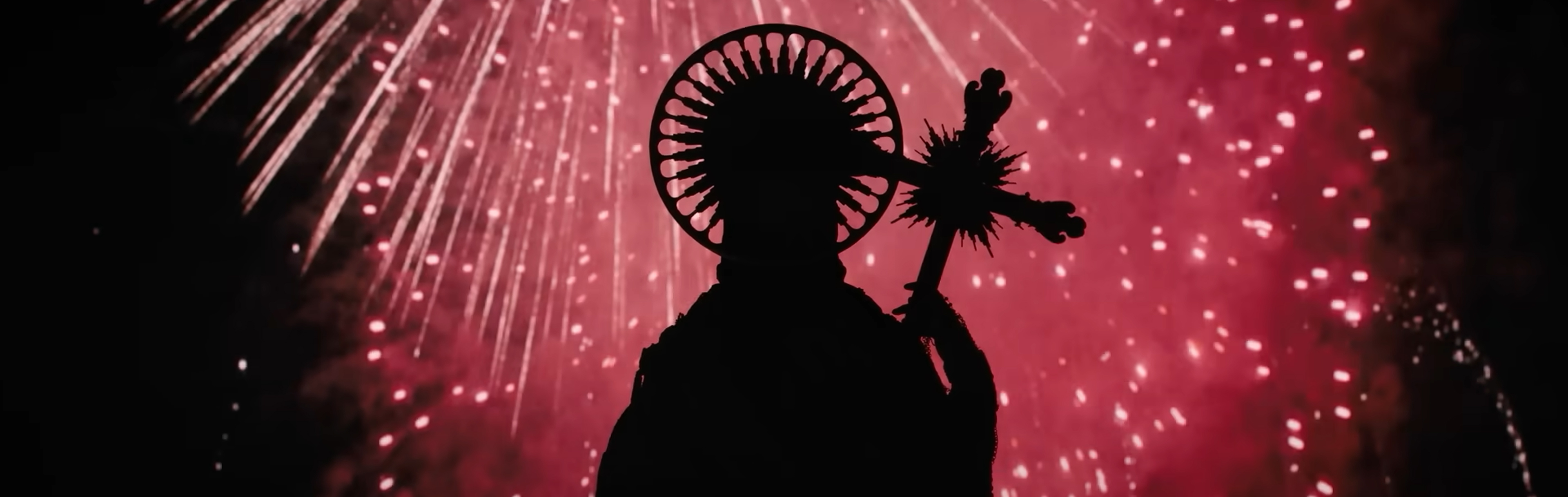 fireworks explode behind a religious statue.